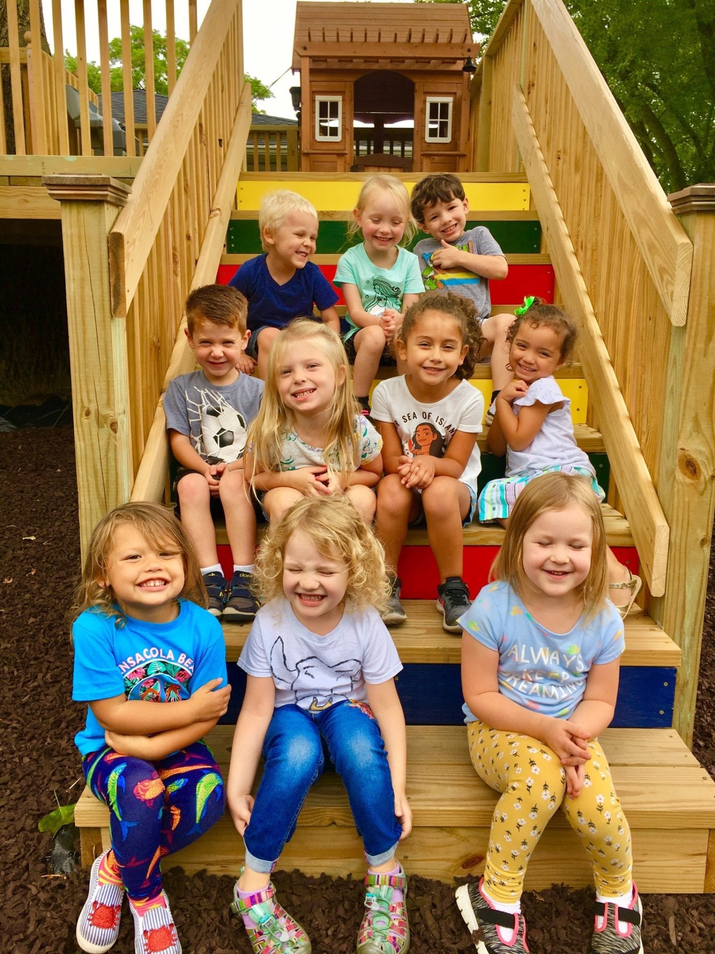 Ten kids sitting on the wooden stairs smiling at the camera